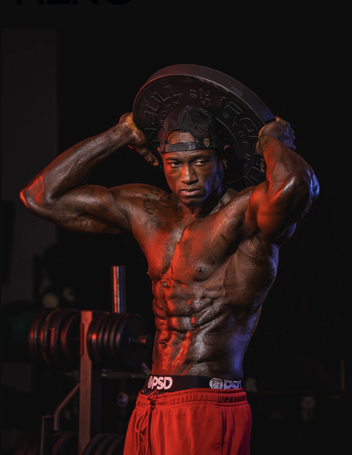 Coach JR holding a weight plate behind his head, mid-movement, muscles tensed